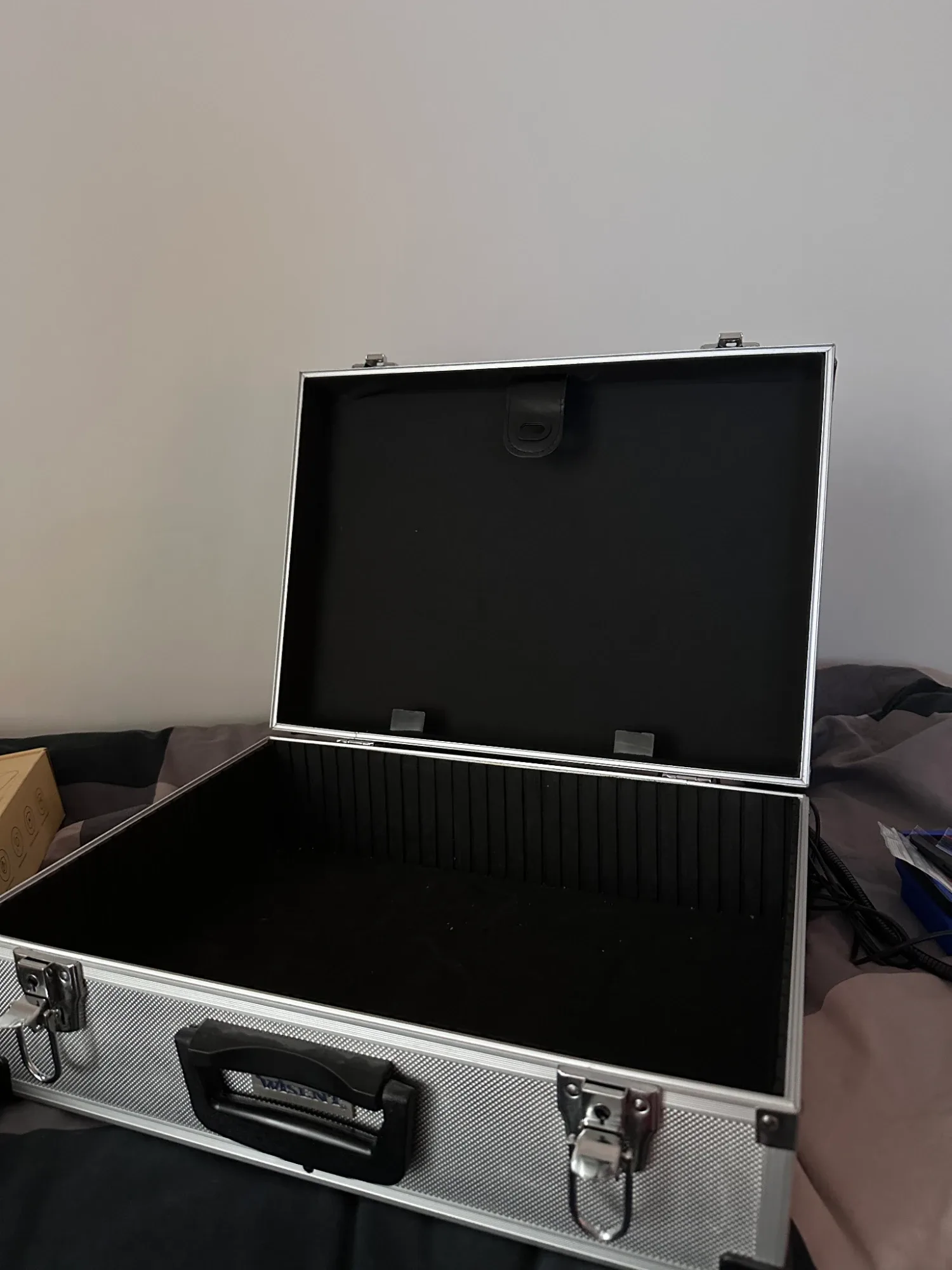 The empty aluminium case standing open, lined in black, with a ribbed divider strip along the back of the base and nothing in it yet.